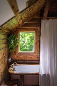 a bath tub sitting under a window next to a wooden wall and floor covered in wood planks