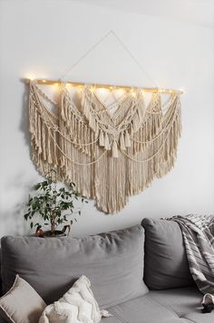 a living room with a gray couch and macrame wall hanging on the wall