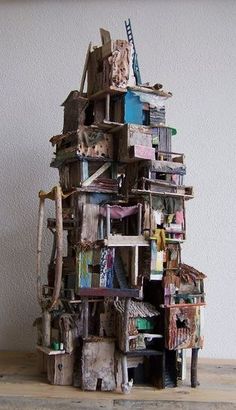 a small wooden structure made out of books on a wood floor next to a white wall