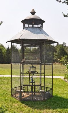 a gazebo in the middle of a grassy area with two birds perched on it