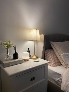 a nightstand with a lamp, books and other items on it next to a bed