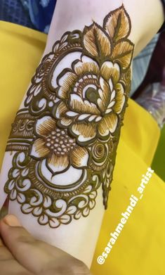 a woman's arm with henna tattoos on it and flowers in the middle