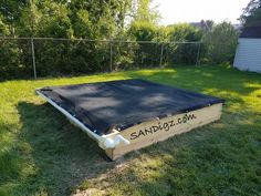 an empty wooden box sitting in the middle of a grassy yard with a black tarp over it