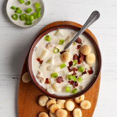 a bowl of soup with crackers and celery on a wooden board next to a white table