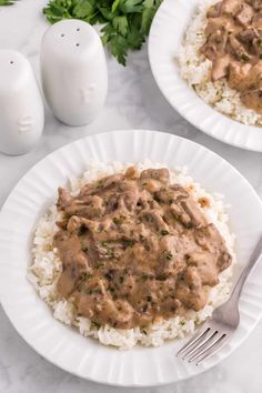 two plates filled with rice and meat covered in gravy