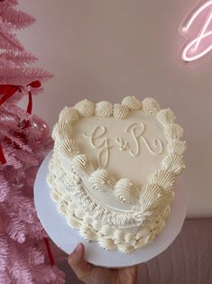 a person holding a cake in front of a pink christmas tree with the initials on it