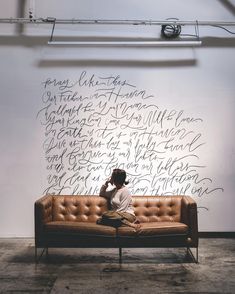 a man sitting on top of a brown couch next to a wall covered in writing