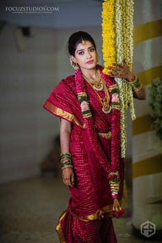 a woman in a red and gold sari with flowers on her head holding a pole