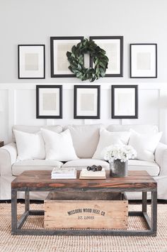 a living room with white couches and pictures on the wall above it, along with a coffee table