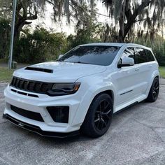 the white jeep is parked in front of some trees