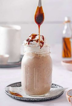 a spoon drizzling sauce into a jar filled with whipped cream and caramel