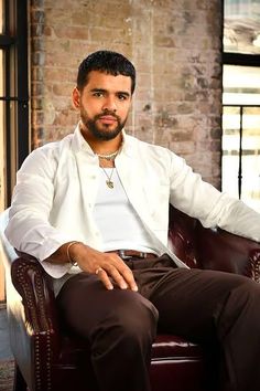 a man sitting in a chair wearing a white shirt and brown pants