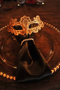 a fancy mask on a glass plate with a black napkin and gold chain around it