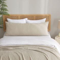 a bed with white linens and pillows in a small room next to a potted plant