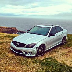 a silver car parked on top of a grass covered field next to the ocean and cliffs