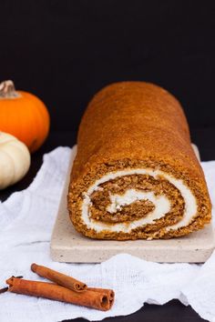 a cinnamon roll on a cutting board next to two pumpkins