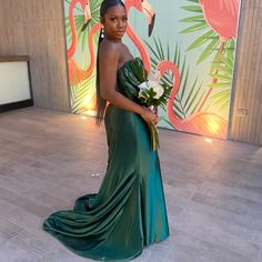 a woman in a long green dress holding a bouquet and standing next to a wall with flamingos on it