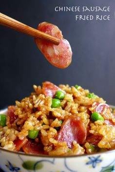 chinese fried rice with bacon and green peas in a blue and white bowl next to chopsticks