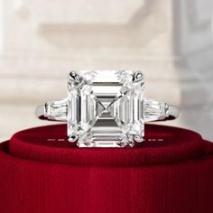 an emerald - cut diamond ring with baguets sits on a red velvet box