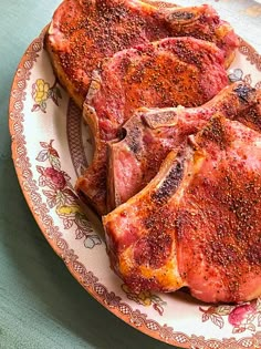 three pieces of raw meat on a plate with flowers around the edges, sitting on a table