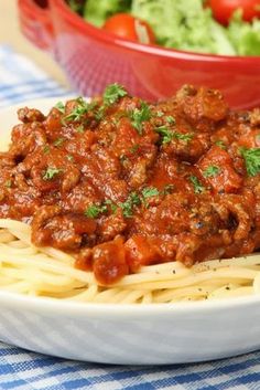 pasta with meat and tomato sauce on a plate next to a bowl of lettuce