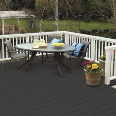 a table and chairs on a deck with potted flowers in the foreground, trees in the background