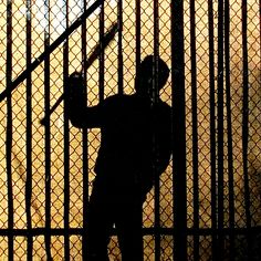 the silhouette of a man holding a baseball bat in front of a fence with bars