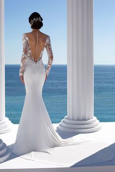 a woman in a wedding dress looking out at the ocean from an outdoor gazebo