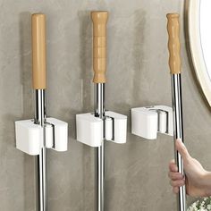 a person is pointing at three wall mounted toilet paper dispensers with wooden handles