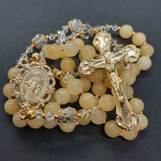 Handmade natural honey jade and Austrian crystal rosary beads. Designed to be used as an aid to praying the rosary. Crucifix and centrepiece are made in Italy. Gold tone INRI crucifix is approximately 2" (50mm) Ornate Miraculous Medal centrepiece is approximately 1 1/4" (25mm). The rosary is made using 8mm natural (undyed) honey jade gemstone beads for the decades.  Honey jade is a pale yellow colour with natural variations in the stones- please check the photos as they form part of the descript Spiritual Gold Rosary With 8mm Beads, Gold Beaded Rosary Bracelet For Healing, Gold Rosary With Gemstone Beads Gift, Yellow Spiritual Rosary As Gift, Gold Rosary With 8mm Beads For Healing, Gold Spiritual Rosary With Gemstone Beads, Gold Gemstone Beads Rosary, Gold Beaded Crucifix Rosary, Gold Spiritual Rosary Bracelet For Healing