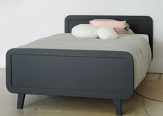 a bed that is made up and has pillows on top of it, sitting in front of a white wall