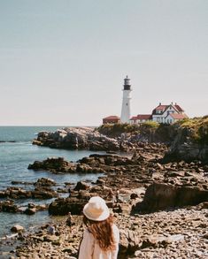 a woman standing on rocks looking out at the ocean and a light house in the distance