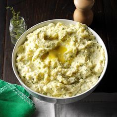 a white bowl filled with mashed potatoes on top of a wooden table next to a green napkin