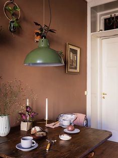 a wooden table topped with plates and cups next to a green light fixture above it