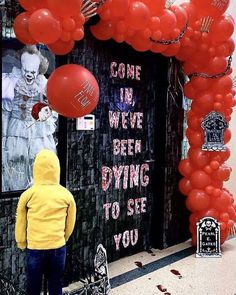 a person standing in front of a building decorated with red balloons and writing that reads come in we've been dying to see you