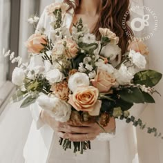 a woman holding a bouquet of white and peach flowers with greenery in her hands