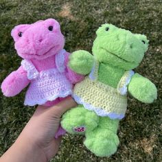 two crocheted stuffed animals are held in someone's hand on the grass