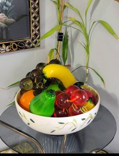 a bowl filled with lots of different colored glass fruit sitting on top of a table