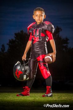 a young boy wearing a football uniform and holding a helmet in the grass at night