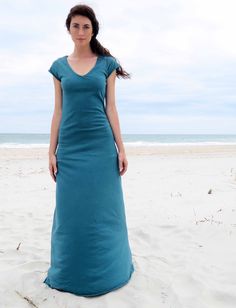 a woman is standing on the beach in a long blue dress with her arms behind her back