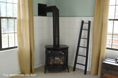 a wood burning stove sitting next to a window in a room with yellow drapes