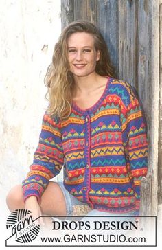 a woman sitting on the ground in front of a door wearing a colorful cardigan