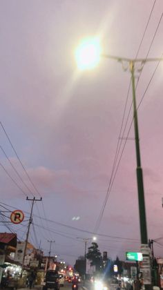 cars driving down the road at dusk with power lines above them and street lights on either side