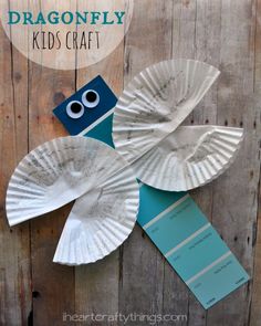 a paper plate bird sitting on top of a wooden table next to a sign that says dragonfly and leaf