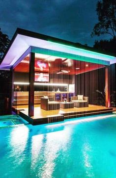 a house with a swimming pool in the middle of it at night, lit up by colorful lights