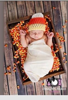 a baby wearing a crochet hat laying in a box filled with corn kernels