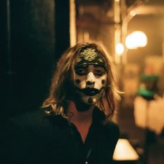 a man with his face painted white and black in a dark room, looking at the camera