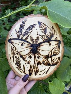 a hand holding up a carved wooden plaque with an image of a butterfly on it