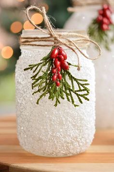 two mason jars decorated with holly berries and twine on a wooden table in front of a christmas tree