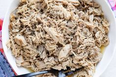 a white bowl filled with shredded meat on top of a colorful cloth next to two spoons